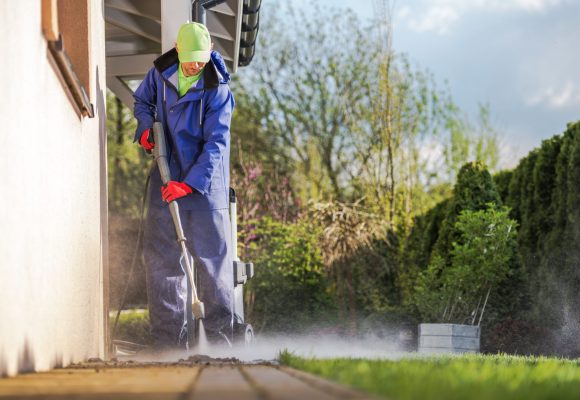 Cleaning House Backyard Brick Paths Using Pressure Washer. Caucasian Men and the Spring Maintenance.